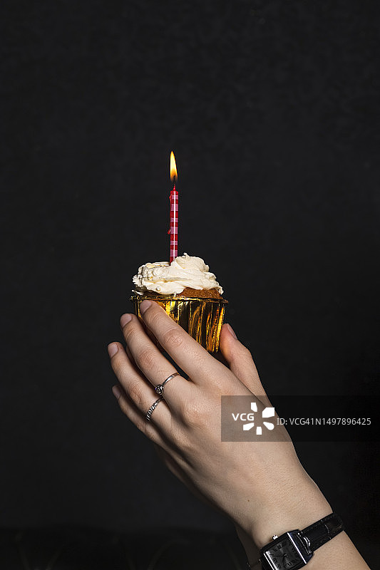 手持带有一根红色蜡烛的小蛋糕，金色包装，黑色背景图片素材