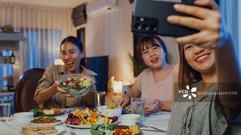年轻的亚洲女性朋友在餐桌旁吃沙拉并进行在线视频通话图片素材