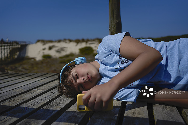 戴无线耳机在木栈道上用手机听音乐的青少年图片素材