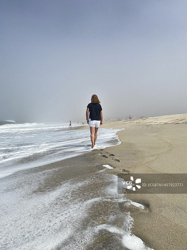 在雾气蒙蒙的海滩上独自漫步的中年妇女图片素材