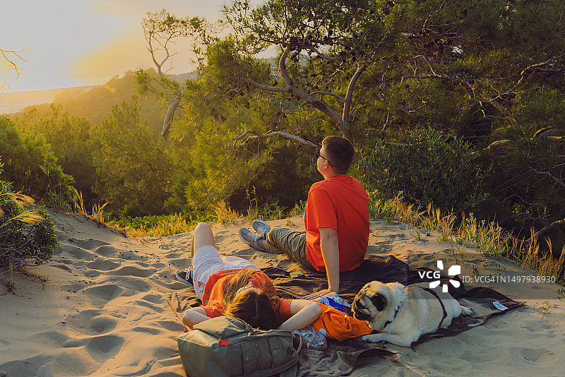 在土耳其帕塔拉，情侣与狗在森林中野餐，欣赏日落海景图片素材
