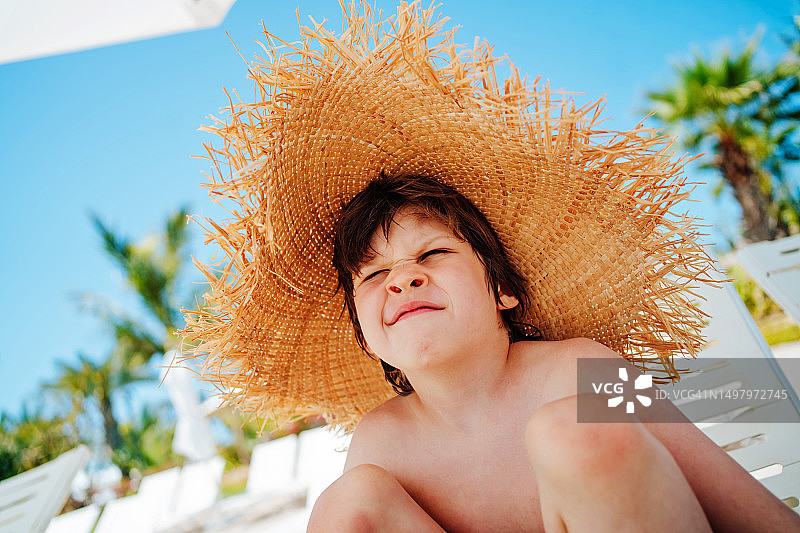 阳光、沙滩和草帽：小男孩在迪拜海滩遮阳伞下放松图片素材