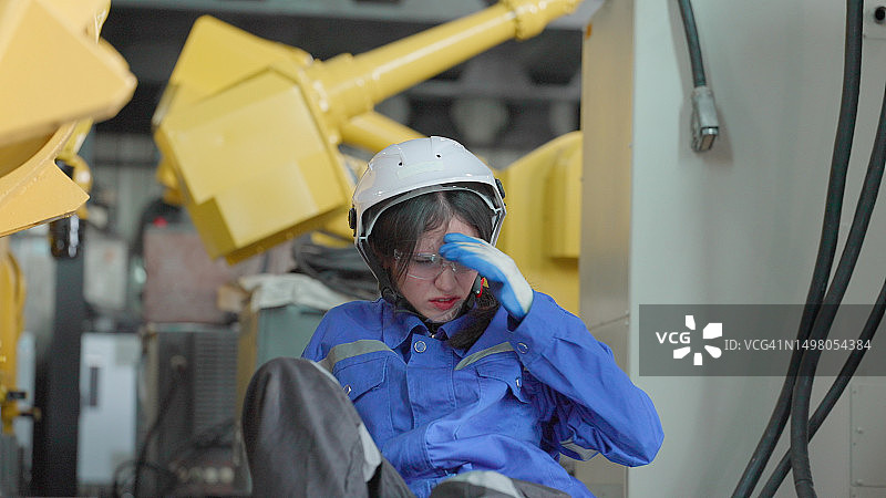 女工因天气炎热晕倒在地，在工厂生产线上检查机械臂的工作系统。工业工厂的职业健康与安全。工伤事故图片素材