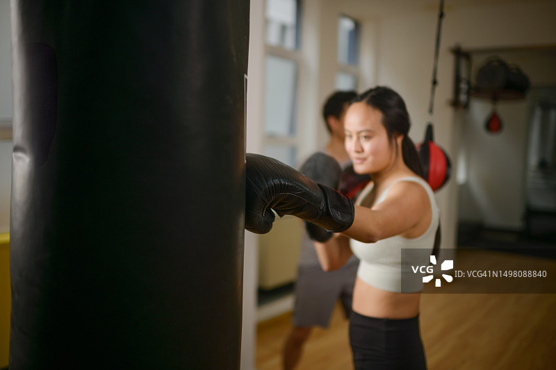 虚焦：年轻中国女人在健身房打拳击，身后有男拳击手图片素材