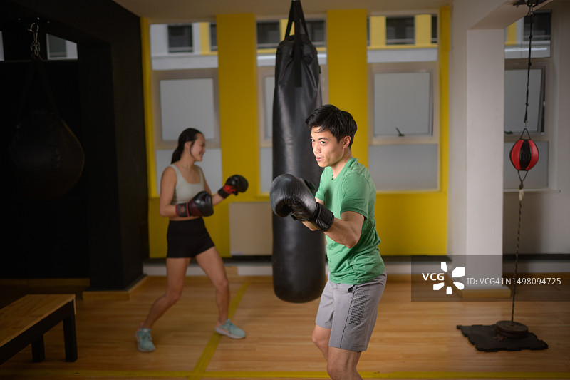 在健身房进行拳击训练的亚洲男子与正在击打沙袋的中国女拳击手图片素材