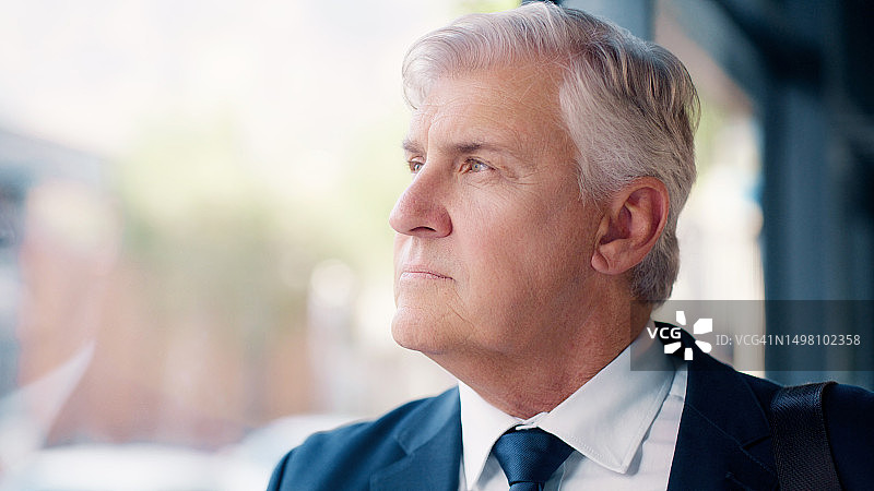 在办公室大楼的窗边平静等候的年长商务男士图片素材