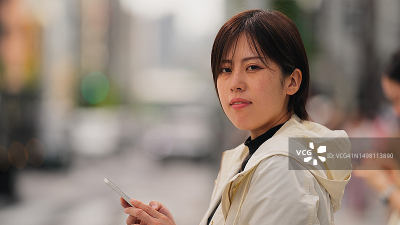 在城市交通信号灯路口等待时使用智能手机的漂亮女人图片素材