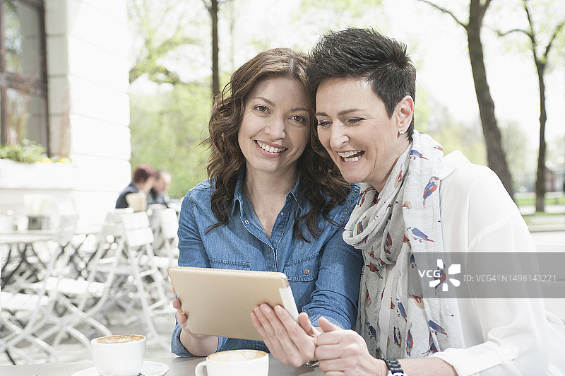 两个朋友在德国巴伐利亚的路边咖啡馆使用平板电脑。图片素材