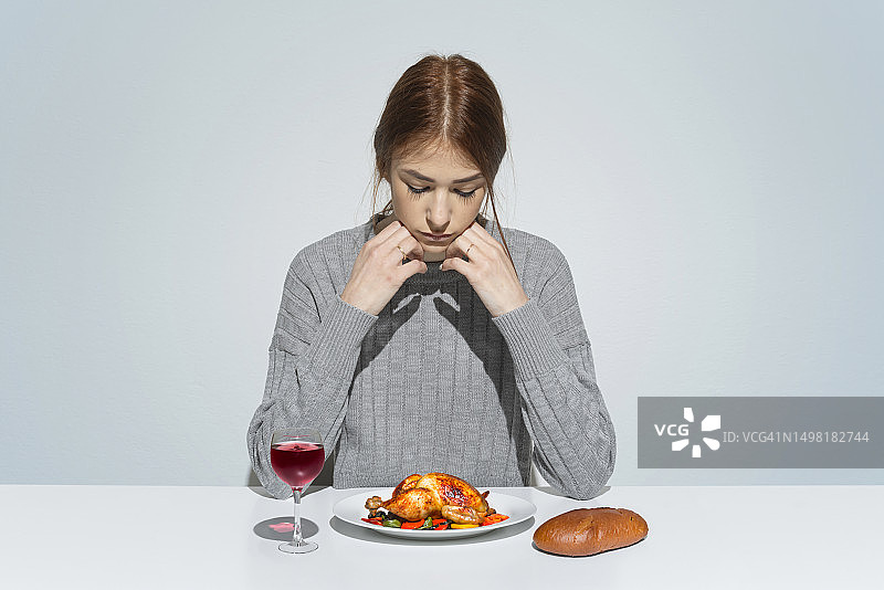 无精打采的女人坐在桌旁吃烤鸡图片素材