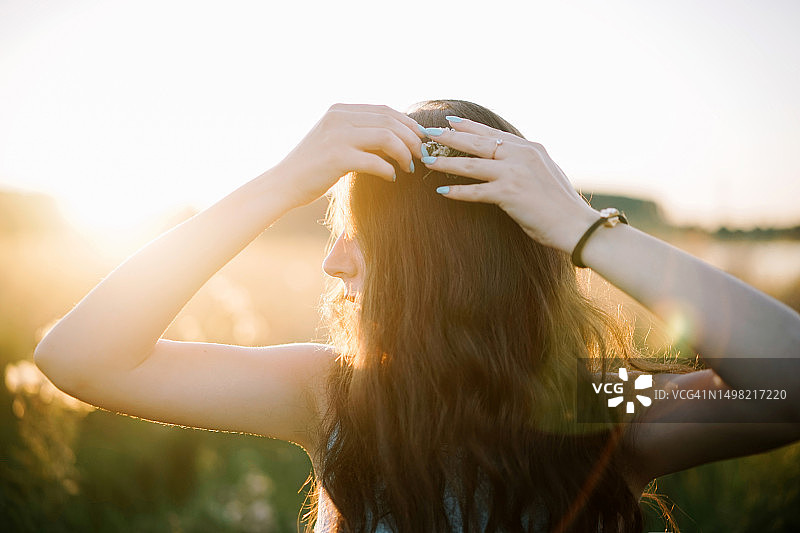 站在西班牙日落天空下，双手放在头发上的女人肖像图片素材