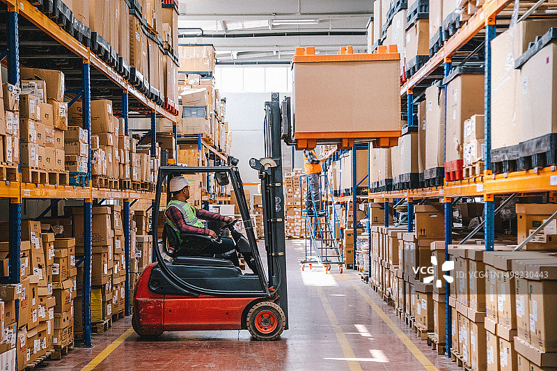 穿制服的工人在工厂仓库中驾驶叉车装载纸箱图片素材