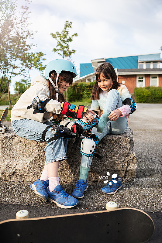 姐妹俩坐下来互相帮助戴上滑板护具图片素材