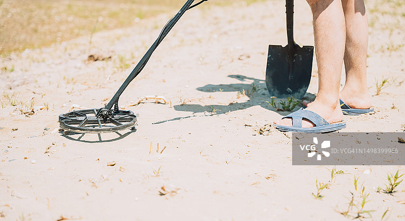 在海滩上用金属探测器和铲子寻找珠宝的男子图片素材