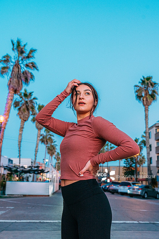 年轻慢跑女性在加利福尼亚州圣地亚哥太平洋海滩附近的街道日落时分回头看的唯美肖像图片素材