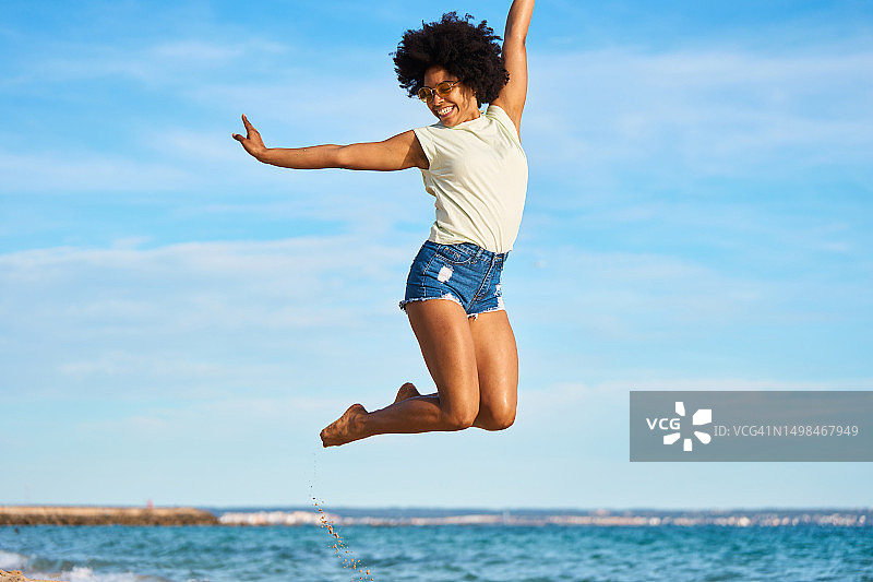 在海滩上举起手臂跳跃的非洲女人图片素材