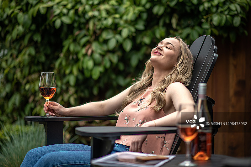 在阿迪朗达克椅上放松，手持玫瑰酒杯的女人图片素材