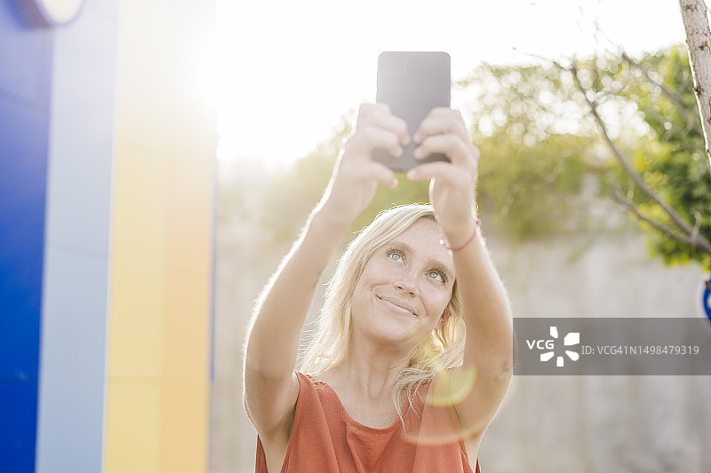 阳光明媚的日子里，年轻女人用智能手机自拍图片素材