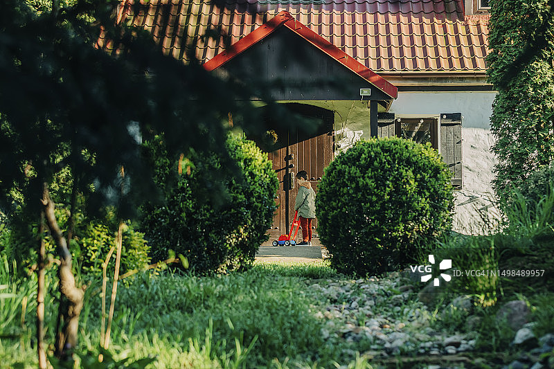 男孩在房子附近玩玩具割草机图片素材