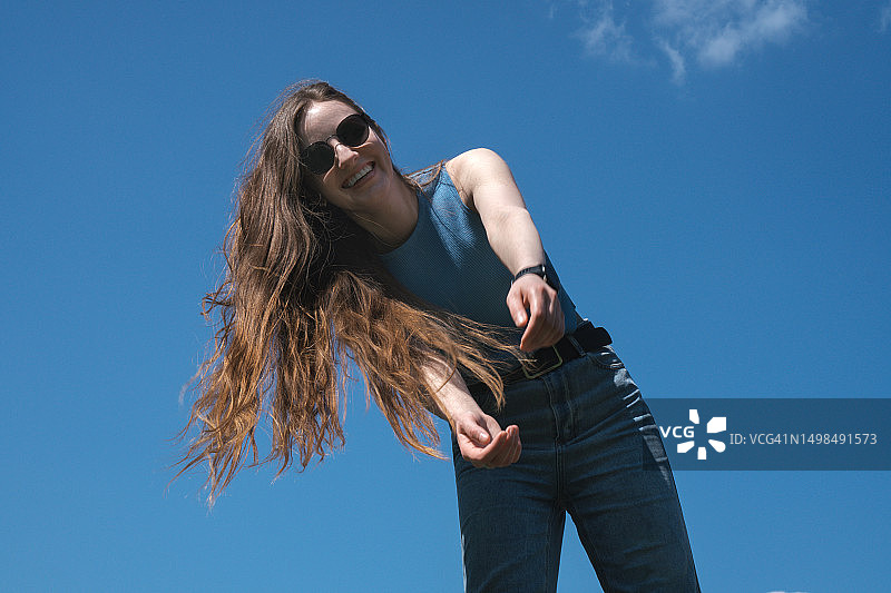 在晴朗蓝天下快乐的年轻迷人女性：享受夏日氛围，明媚生活方式摄影图片素材