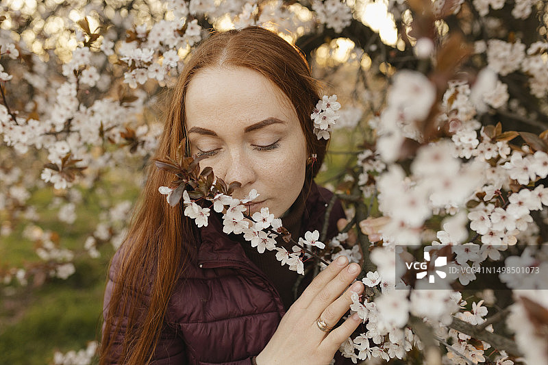 红发女人在公园里闻树上的花图片素材