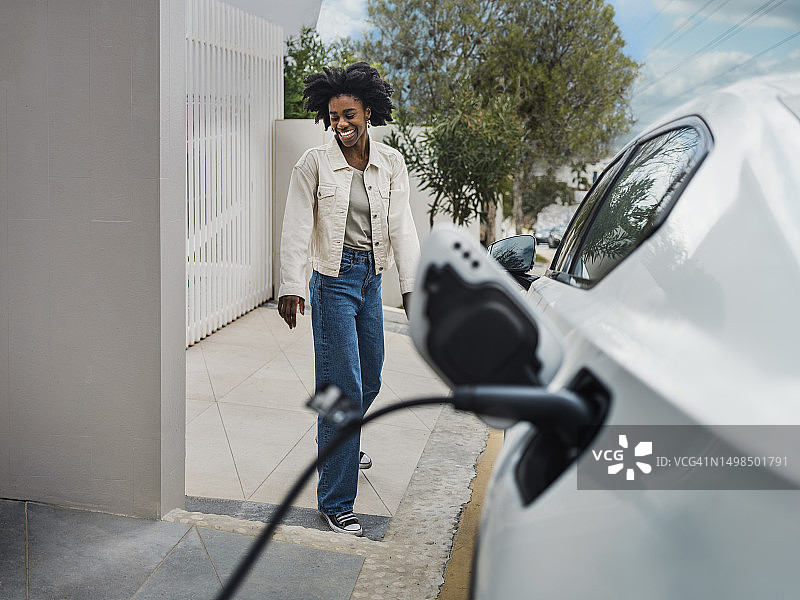 在充电站旁的电动汽车旁微笑的年轻女人图片素材