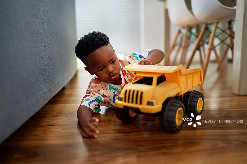 在家中硬木地板上玩翻斗车的可爱男孩图片素材