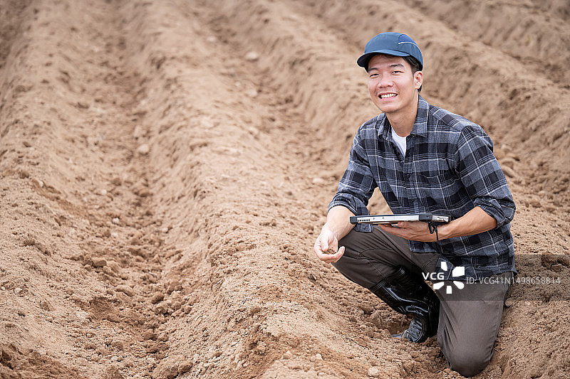 改善土壤肥力是智能农业运营中最大的成本节约部分。一位日本男性生物学家在高角度视图中，通过平板电脑检查和收集耕作过程中土壤健康和肥力质量。图片素材