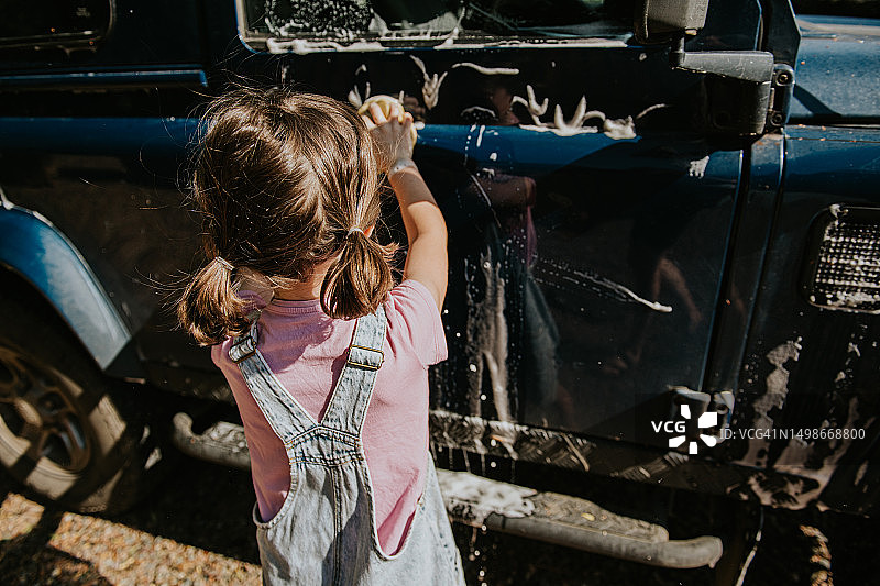 小女孩用黄色海绵清洗蓝色汽车图片素材