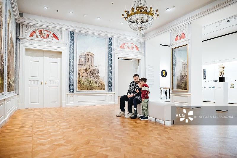 父亲和两个年幼的孩子坐在博物馆里图片素材
