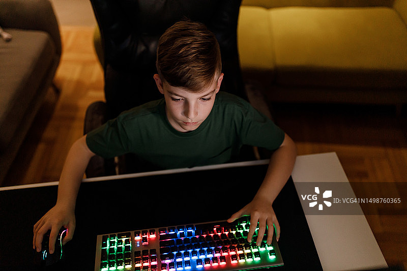 男孩晚上在客厅里用RGB游戏键盘玩电子游戏图片素材