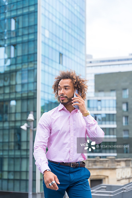 在彩色建筑的商业区外，拥有非洲发型的拉丁裔企业主或公司经理在办公室外打电话图片素材