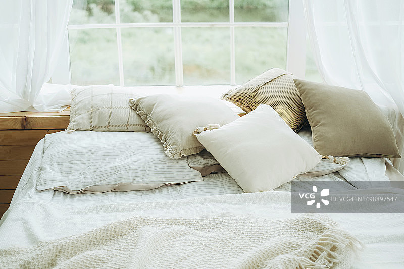 床上靠垫、枕头、毯子和格子布，背景是窗户图片素材