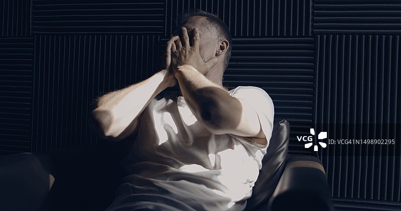 沮丧的男人独自在黑暗的房间里捂着脸图片素材