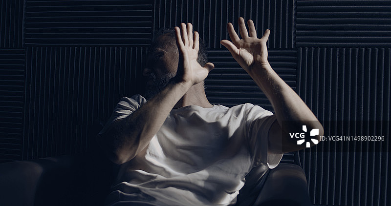 沮丧的男人独自在黑暗的房间里，坐在窗边躲避光线，用手遮住脸图片素材