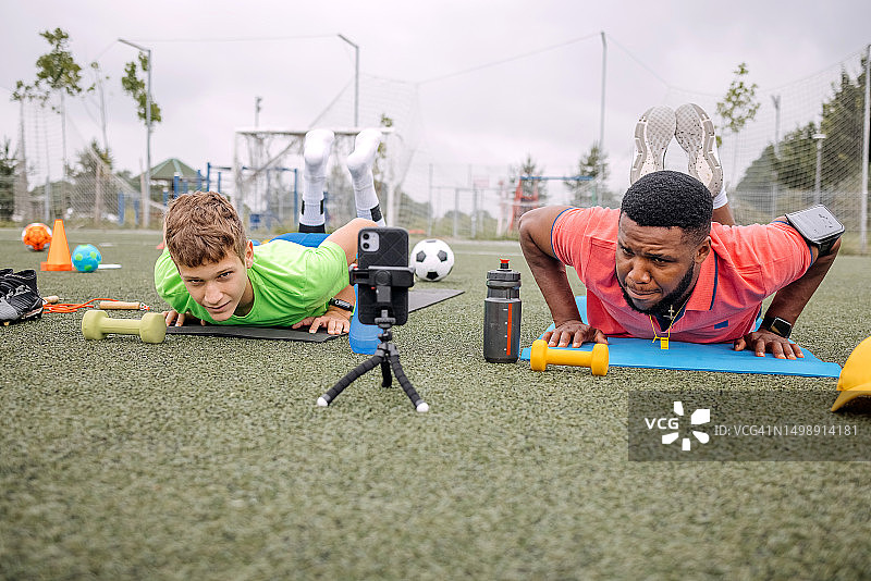男孩在黑人教练的指导下进行俯卧撑训练图片素材