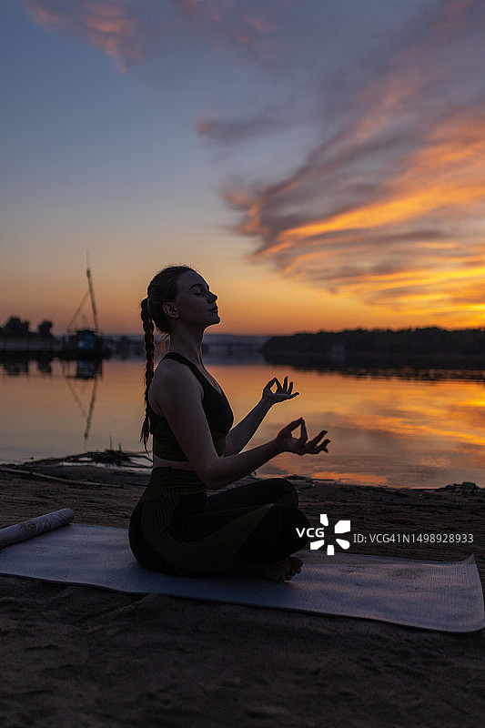 穿着运动服的优雅女运动员在海滩水边莲花坐姿侧视图图片素材