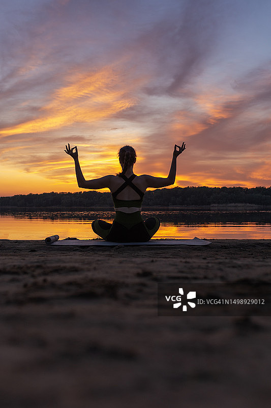 年轻女子在日落时分以莲花坐姿，举起双手冥想图片素材