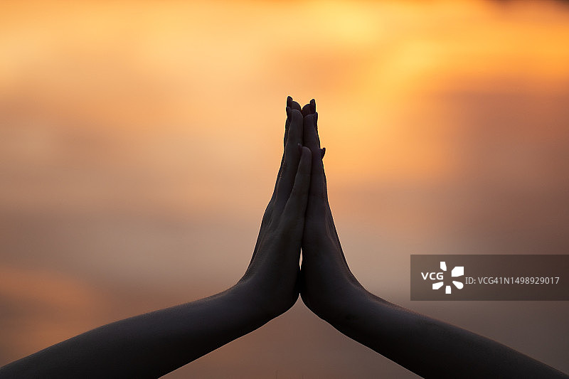 瑜伽教练的双手合十特写，背景是模糊的日落天空图片素材