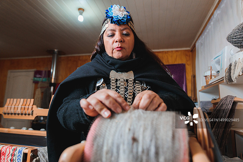 在纺织作坊里用滚筒梳理机加工羊毛的马普切族女工图片素材