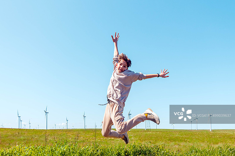 男孩在风力涡轮机农场前跳跃图片素材