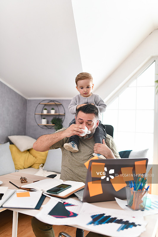 父亲在办公室喝咖啡工作，儿子坐在肩膀上图片素材