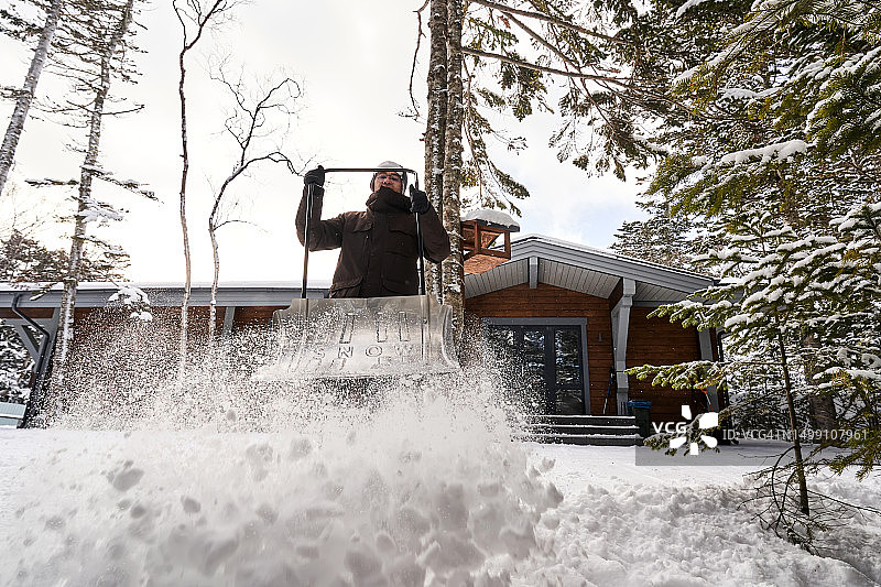 男人在自家房子附近清理积雪图片素材