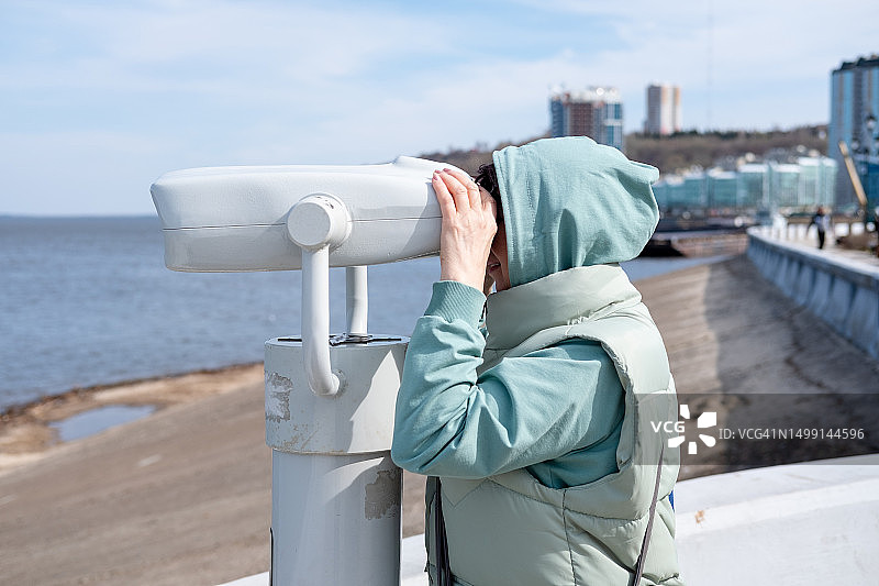 戴着头巾的女人在海边用望远镜观赏美景图片素材