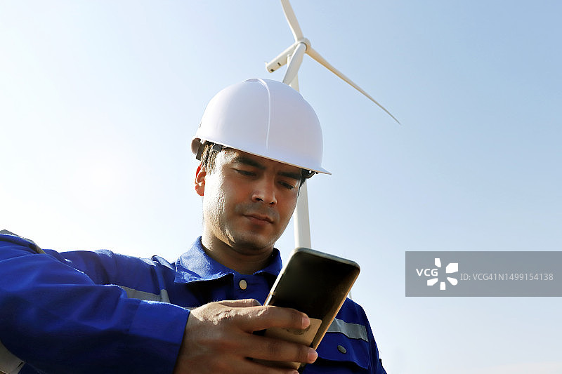 工程师站在风力涡轮机旁的田野里使用手机图片素材
