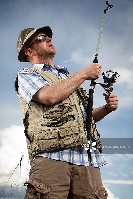 渔民手持钓竿，以多云天空为背景图片素材