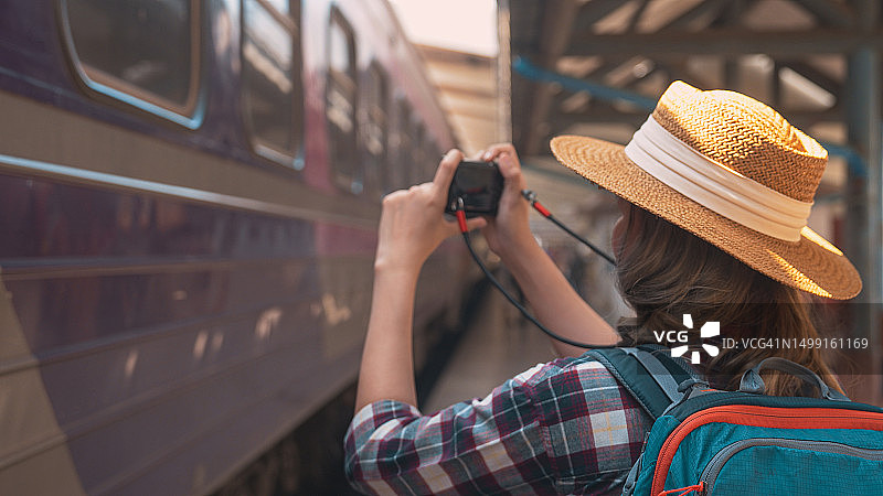 年轻亚洲女游客背着背包在铁路上。女游客用相机拍摄火车侧面，活跃的旅行生活方式概念图片素材
