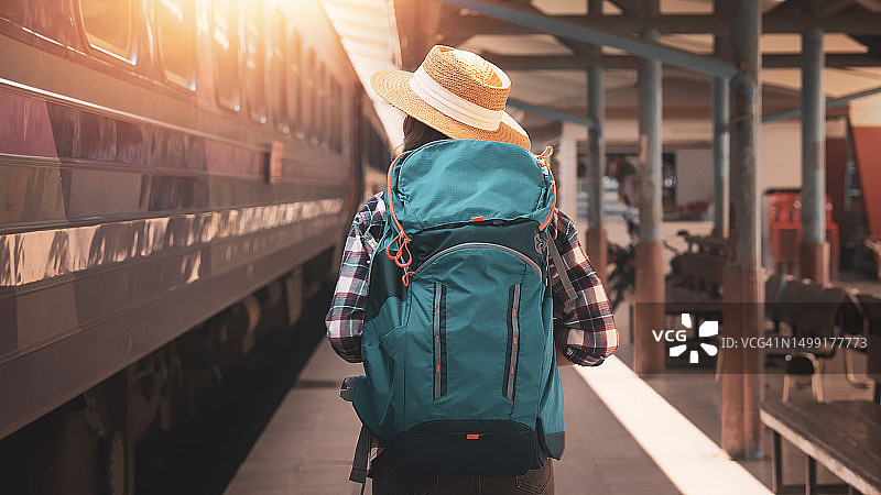 女游客在火车站行走。年轻的亚洲女游客背着背包在铁路上。火车站的背包和帽子与旅客。旅行概念图片素材