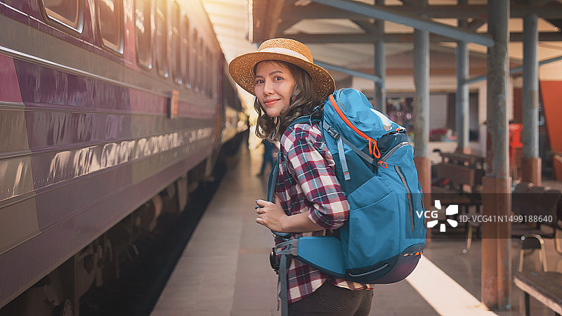 女游客在火车站行走。年轻的亚洲女游客背着背包在铁路上。火车站的背包和帽子与旅客。旅行概念图片素材