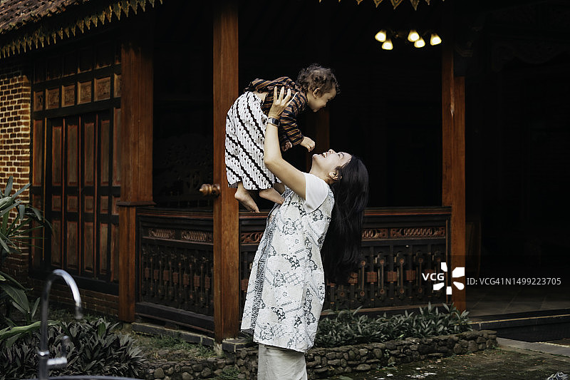 亚洲母亲和儿子（穿着日惹传统服装）在他们的爪哇传统房屋里玩耍图片素材