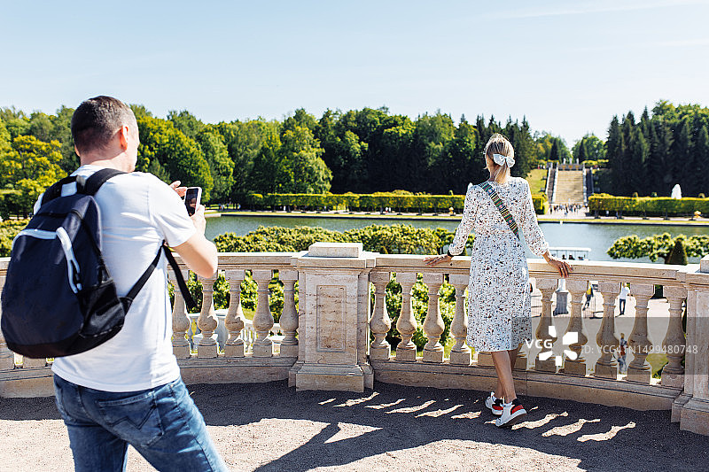丈夫在夏日拍摄站在彼得霍夫公园露台栏杆附近的妻子，可欣赏湖景图片素材